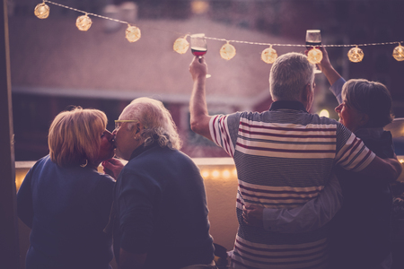 Romantic and love concept with two senior adults couple celebrate together at home in a terrace with city view - toasting with wine and kissing - matures people have fun in friendship outdoorの写真素材