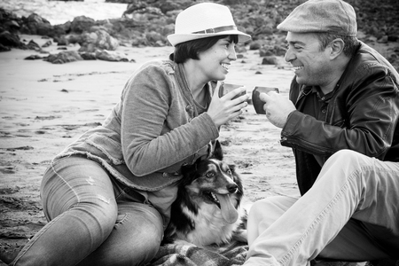 Black and white image with happy couple in love sitting and enjoying leisure activity outdoor drinking together with nice border collie dog in the middleの写真素材