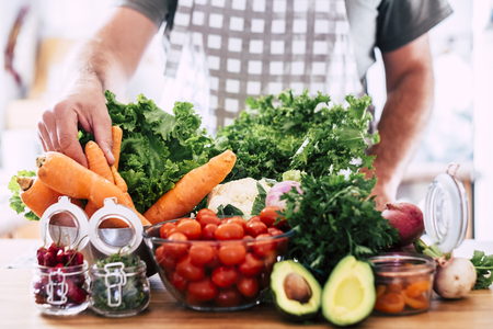 Man preparing vegetarian and vegan food - table full of fresh seasonal healthy vegetables - mix of colors and vitamin - focus on hand taking a carrot - wellnesss lifestyle conceptの写真素材