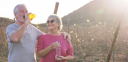 Man and woman caucasian people in outdoor leisure sport activity together - aged elderly concept - drinking energetic drink together - backlight in sunny day perfect for outside activitiesの写真素材