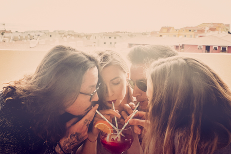 Group of friends two couples men and women celebrate and have fun together drinking from the same glass - party event time in friendship for caucasian people - new year outdoor celebrationの写真素材