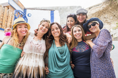 Group of middle aged young women stay together in front of the camera enjoying friendship - cheerful ladies with coloured dress smile and enjoy the outdoor leisure activityの写真素材