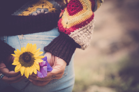 Hippy wanderlust travel concept image with back of girl with blue jeans taking a yellow sunflower - coloured sweater and bokeh background for dreaming concept contentの写真素材