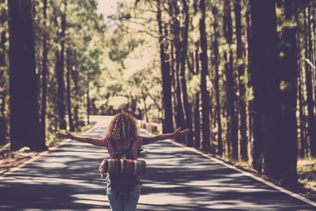 Eternity and success satisfaction life concept with lonely girl curly hai rin the middle of long road in the forest with open arms and backpack - wanderlust and travel style peopleの写真素材