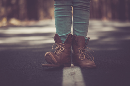 Travel wanderlust lifestyle concept with pair of broken trekking shoes closeup in the middle of an asphalt long road - defocused background - vintage filter and dark tonesの写真素材