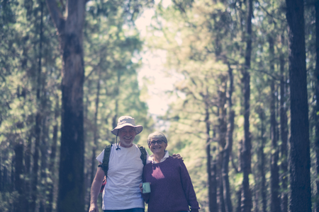 Happy caucasian senior couple smile and enjoy the travel with backpack in the outdoor nature forest - alternative free vacation concept for aged people - joyful lifestyle and hug and loveの写真素材