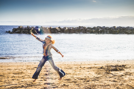 Happiness and feedom in vacation concept with nice curly middle age youth woman jumping at the beach enjoying the leisure outdoor activity in the nature with blue sea in backgroundの写真素材