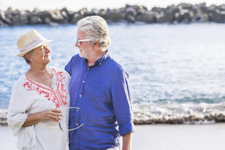 Retired happy couple at the sea during vacation - smiling people with ocean in background and outdoor leisure activity together forever in love and relationshipの写真素材