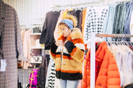 Attractive fashion young beautiful cute woman in a store wearing a ecological natural fur with many colors - modern and chic people in commerce concept - city lifestyle consumismの写真素材