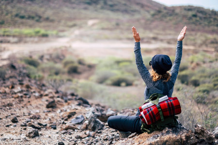 Rear view of woman with blonde curly hair doing yoga position and meditate during travel trekking...