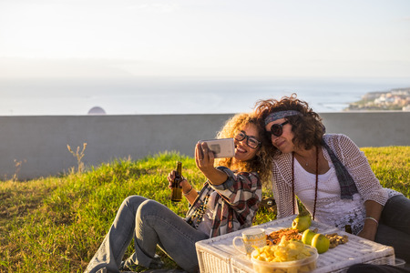 Cheerful cpule of middie age adult ladies enjoying picnic outdoor and taking selfie picture to share onloine lifestyle with internet and technology - hipster and hippy style and happy for leisure activity with a viewの写真素材