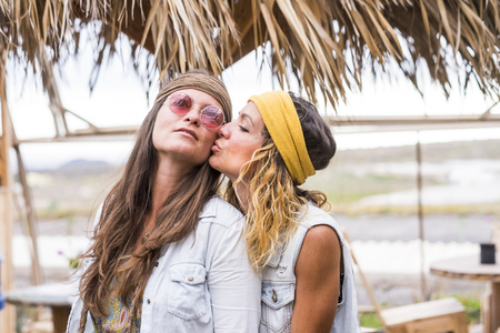 Couple of young woman kissing eachother with love and romance in outdoor place with chairs and tables - same sex love - hippy freedom style concept for people alternatve lifestyle -の写真素材