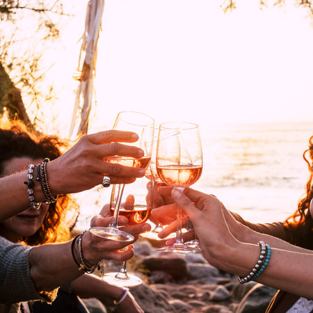 people drinking at party outdoor. group of friends white wine in hand toasting with glasses. close...