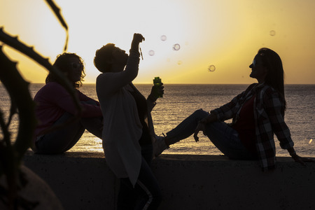 Friendship for women during the sunset - emotion and feeling with golden colors and three ladies in silhouette playing with bubbles soap - vacation and outdoor leisure activity conceptの写真素材