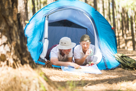 Caucasian traveler adult couple lay down inside a tent while choose and plan on a map the next step of their journey - nature lifestyle leisure activity for alternative retired peopleの写真素材