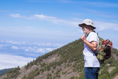 Lonely adult aged trekker with backpack standing and looking at the beautiful landscape at the mountains - trekking and hiking for mature people in outdoor leisure activity - travel and blue sky in backgroundの写真素材