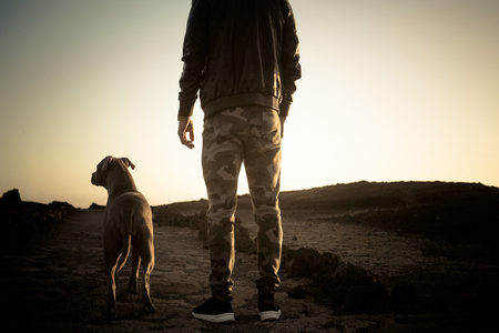 Lonely man and best friend dog walking together on a path in outdoor desert leisure activity with ocean in background at the end - friendship and travel concept for people with animalsの写真素材