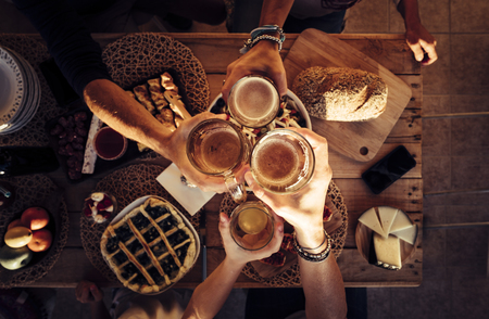 People eat mixed meals at festive table served for party. Friends celebrate with food on wooden table top view. Happy company having lunch, clinking glasses - outdoor friendship conceptの写真素材