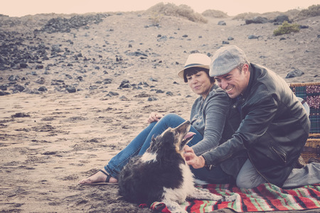 Alternative vintage style colors couple having fun in outdoor leisure activity picnic with adorable puppy dog - pet therapy concept for cheerful middle age caucasian people enjoying the love for animalsの写真素材