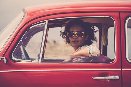 Serious lady on a old retro nice red car looking at you with open window glass - traveler with hippy freedom lifestyle and alternative vehiclesの写真素材