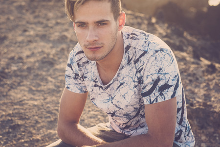 Beautiful trendy millennial young blonde model caucasian people sitting outdoor and loooking straight - sun and sunset in background - warm light from behind and defocused backgroundの写真素材