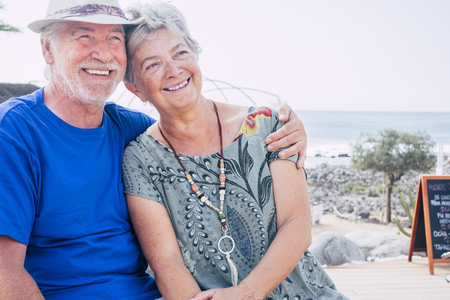 Happy senior couple laughing hugged on a summer day. concept of vacation, relaxation, rest. Behind it as a sea, ocean background - Cheerful caucasian aged people in outdoor leisure activity togetherの写真素材
