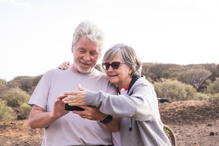 Cheerful caucasian adult senior couple with mountain bike doing healthy sport outdoor leisure activity together - Old people enjoy elderly riding in the nature and enjoying lifestyleの写真素材