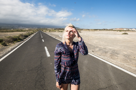 Beautiful attractive caucasian girl walk with a fashion dress on a long way road - horizon and travel concept with airplane flying in the background. and asphalt to infinite - future for people conceptの写真素材