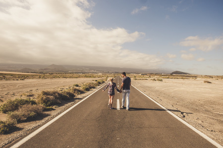Young couple walk together on a long straight road in the middle of a desert nowhere place - life and love and relationship concept with youth people walking hand to hand - summer timeの写真素材