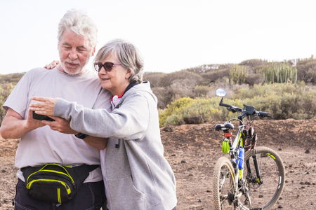 Adult mature caucasian couple smile and enjoy the outdoor sport activity with mountain bikes while check maps and paths on cellulaer internet connected phone - technology and healthy lifestyleの写真素材