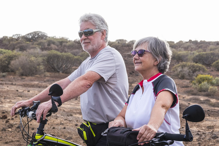 Cheerful caucasian adult senior couple with mountain bike doing healthy sport outdoor leisure activity together - Old people enjoy elderly riding in the nature and enjoying lifestyleの写真素材