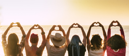 Group of diversity alternative young woman enjoying the sunset at the sea doing hearth symbol with hands - people enjoying friendly lifestyle - vacation in friendship concept for femalesの写真素材