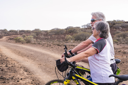 Caucasian adult senior couple with mountain bike doing healthy sport outdoor leisure activity together - Old people enjoy elderly riding in the nature and enjoying lifestyleの写真素材