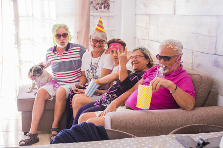 Group of mixed ages people from grandfathers to teenager having fun during birthday celebration together - family at home concept with carnival stuffs and masks - diversity people lifestyle with seniors and youngの写真素材