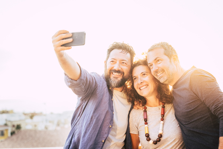 Bright yellow filter group of caucasian 40 years old people men and woman taking selfie picture with smart phone device - backlight and white sky in bnackground - happy leisure activity tonceptの写真素材