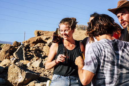 Group of friends enjoying a beer together in outdoor rocky space - summer time concept and fun for young people in friendship - caucasian boys and girls leisure activityの写真素材