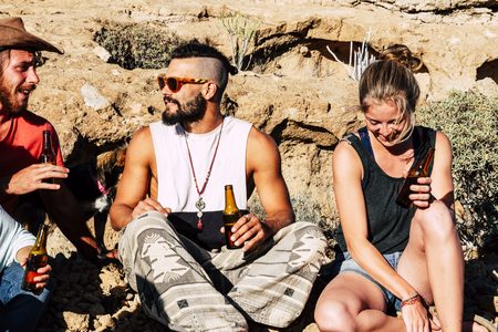 Friends enjoying the summer day together sit down on the rocks drinking beers together in friendship - people have fun with easy lifestyle - less is more conceptの写真素材