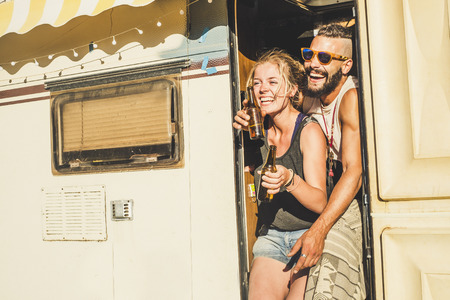 Young cheerful couple laughina lot and having funtogether on the door of a old vintage caravan - alternative vacation concept for happy people - sunny day of vacation concept for travelersの写真素材