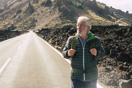 Adult aged senior man walking with backpack in long road at the mountain enjoying the alternative vacation trip and living a lifestyle adventure - retired people in outdoor - tourist conceptの写真素材