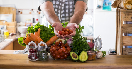 Vegetarian and healthy food lifestyle at home concept - table in the kitchen full of mixed coloured vegetables and man hands showing you the freshness - background and energy infredients to cookの写真素材