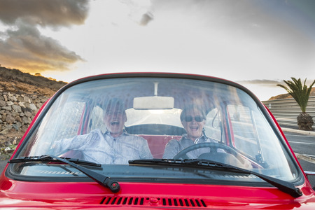 nice adult couple hug and love inside a red old vintage car parked on the road. smiles and have fun traveling together. happiness and lifestyle for nice people. summer time and vacation journeyの写真素材