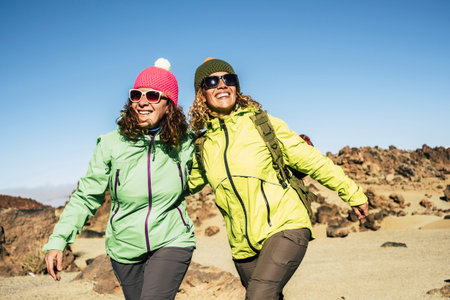 Happy cheerful couple of middle age women friends walking together at the mountain for alternative vacation - sunny day in outdoor leisure activity in the nature - happiness and joyful lifestyle for peopleの写真素材