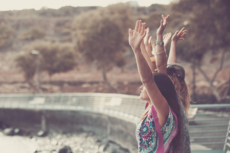 Group of coloured diverstiy clothes girls giving up hands enjoying the independence and freedom together, in friendship - love and peace concept for modern hippy women -の写真素材