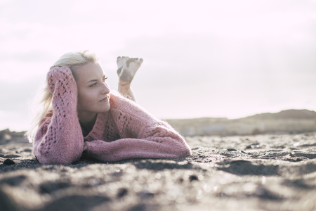 Attractive lady lay down at the beach on the sand in winter or autumn season with a pink sweater enjoying the outdoor relaxed activity alone with no people around -millennial girl feel the worldの写真素材