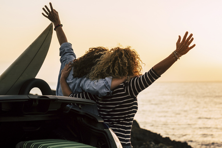 Happy couple of curly girl have fun together and look at the sunset in front of the ocean in tropical beautiful vacation outdoor - hug and friendship for happy peopleの写真素材
