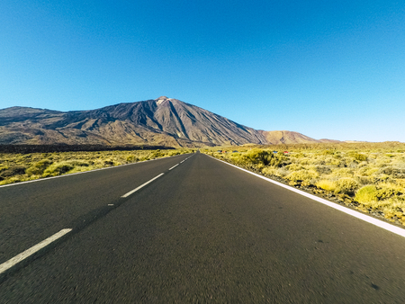 Long way road at the mountain with vulcan mount in front and blue clear sky - ground point of view with black asphalt and white lines - driving and travel conceptの写真素材