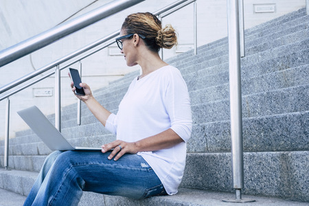 Business woman beautiful female working with phone device and laptop computer aoutdoor witting on a urban stairs in the city - digital nomad and freelance - freedom to work outdoor and enjoy modern happy lifestyleの写真素材