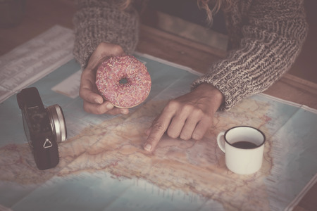 Close up of traveler woman hands planning the next trip vacation with a paper map - old camera and coffee on the table - breakfast time with donuts - travel and vacation conceptの写真素材