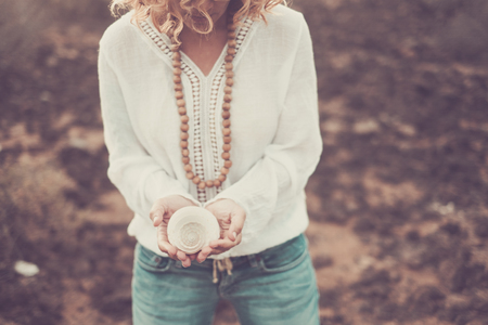 Unrecognizable curly long hair woman taking a shell with desert in background - environment and nature protection concept with caucasian fashion chic people outdoorの写真素材