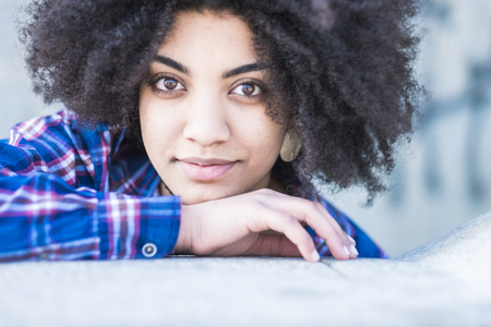 Cute beautiful brunette curly afro hair looking at the camera and smile a little bit - fashion casual millennial style young woman - attractive girl portrait outdoorの写真素材